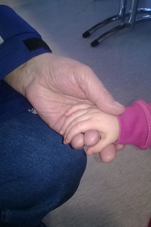 Vanhuksen ja lapsen käsi toistensa kädessä.